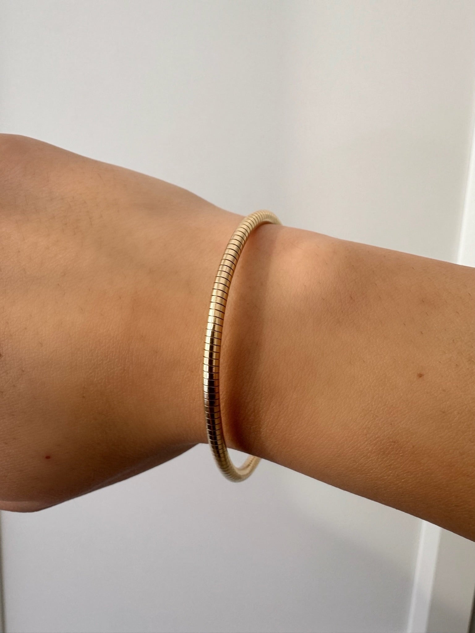 A thin gold snake-bone style bangle bracelet worn on a person's wrist, shown against a plain light background.